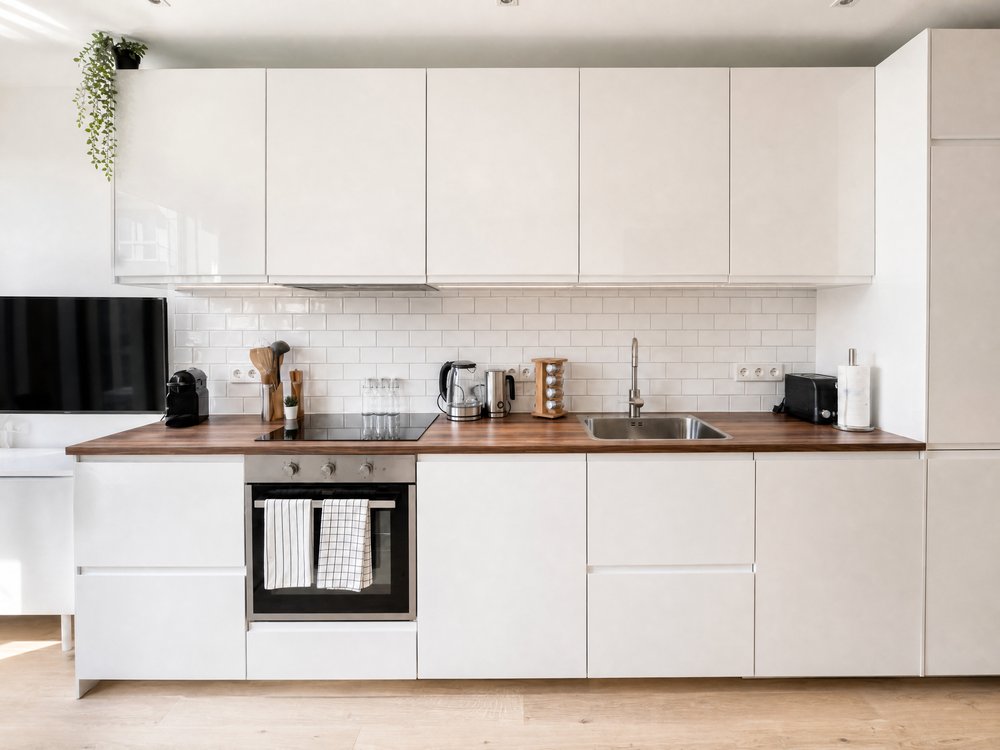 Full-length white kitchen with walnut worktop, white metro tile splashback and handleless cabinets in renovated studio apartment Oud-Zuid Amsterdam - Ruimte interior design