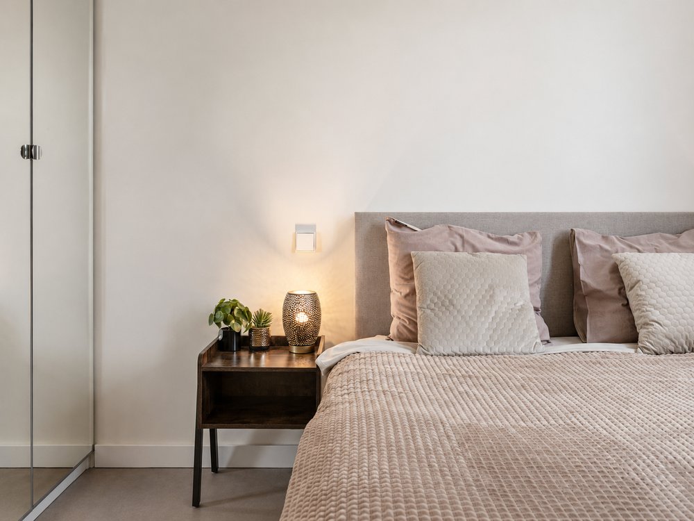 Bedroom detail with upholstered headboard, layered cushions and warm bedside lighting, Riga Kīpsala - Ruimte interior design