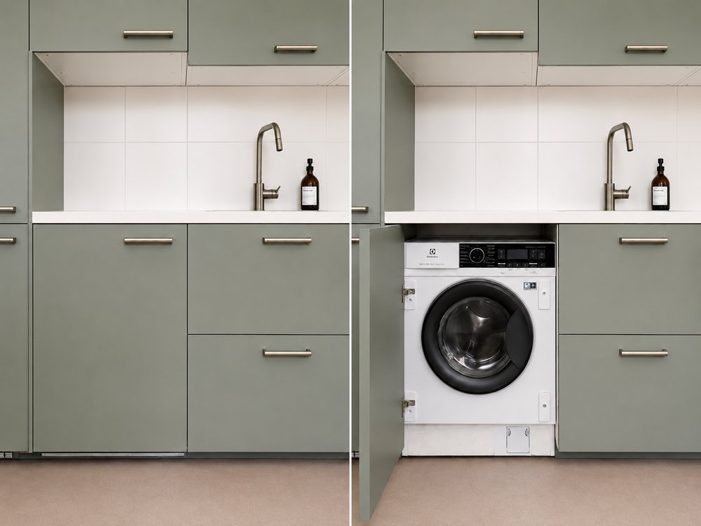 Sage green kitchen cabinetry open to reveal integrated washing machine in base cupboard, pied-à-terre Kipsala Riga — Ruimte interior design