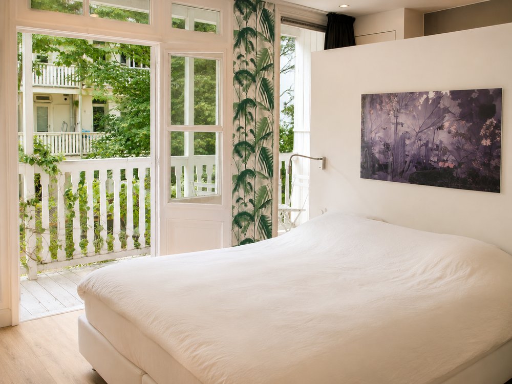 First floor bedroom with full-height garden doors opening to balcony, botanical curtain panel and white bedding, Oud-West Amsterdam - Ruimte interior design