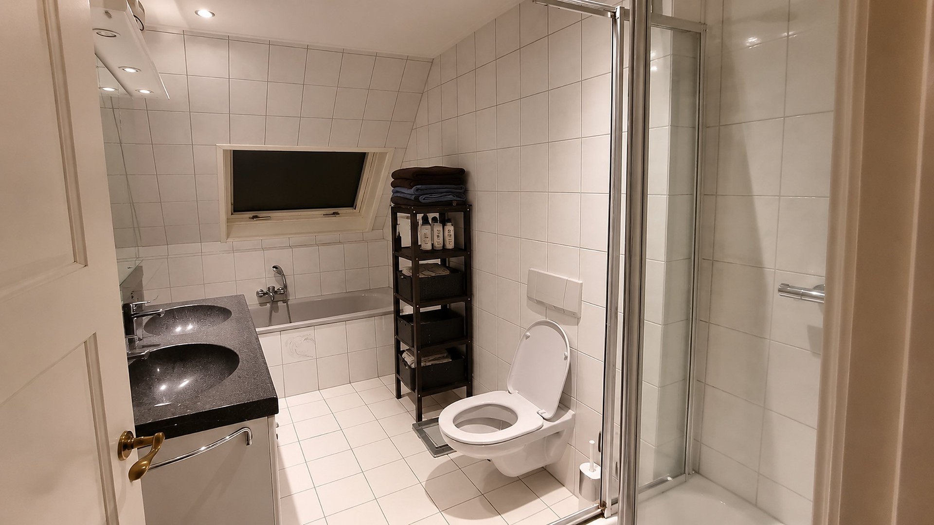 Attic bathroom in Bussum before renovation, with white square tiles, dated double basin, corner shower and small skylight