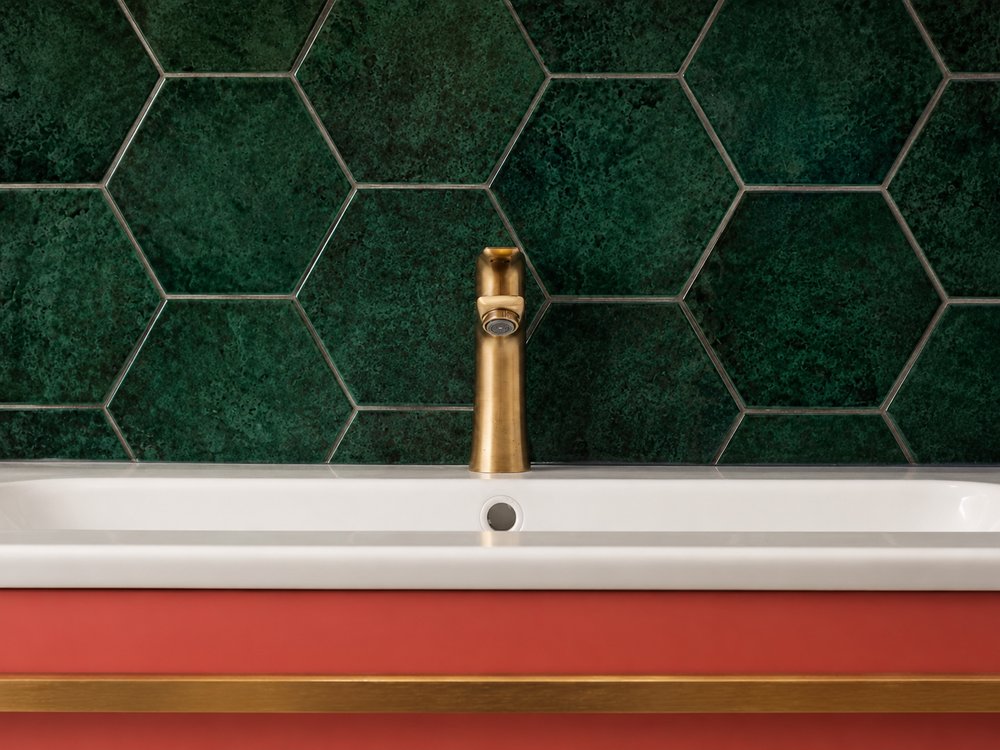 Close-up of brushed brass basin tap against deep green hexagonal wall tiles, Bussum bathroom - Ruimte interior design