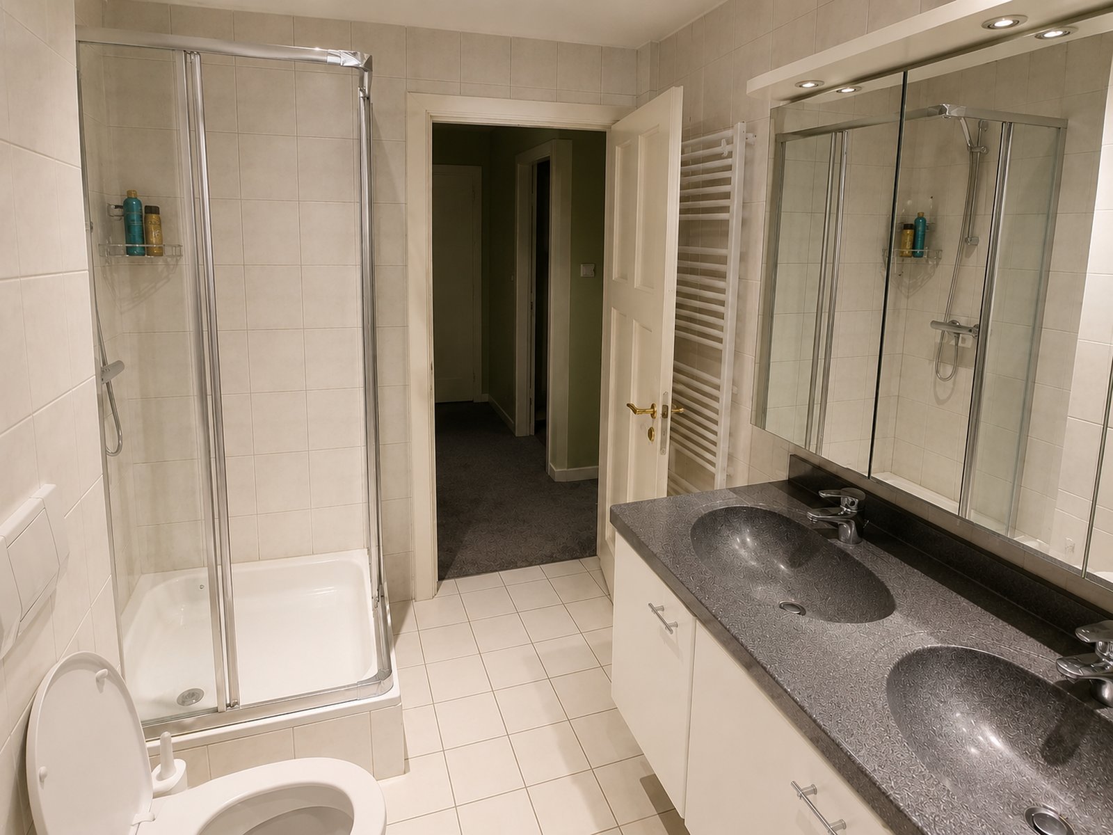 Ground floor bathroom before renovation in Bussum, with beige square tiles, corner shower, double granite basin and ceiling spotlights